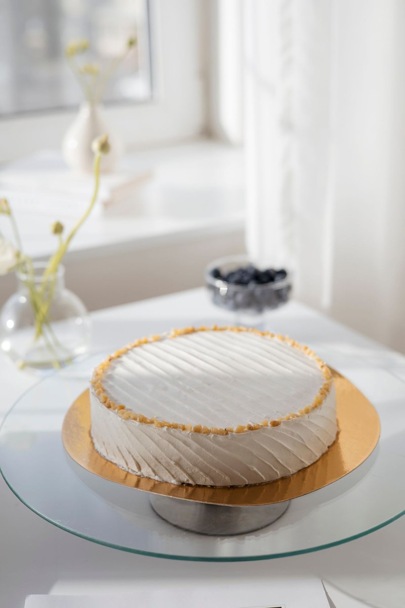 White frosted cake with nut border on a glass cake stand