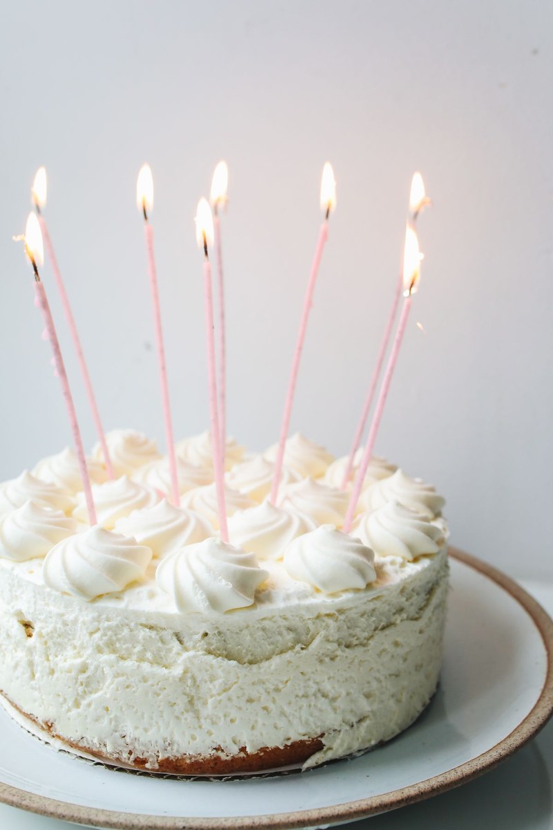 White frosted celebration cake with tall lit pink candles on a ceramic plate